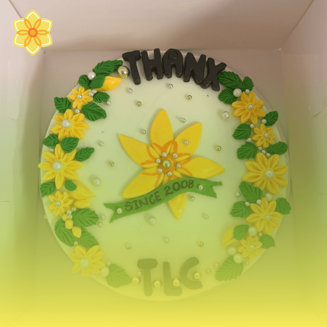 The thank you cake Lanka baked for the team, reading "THANX TLC", with a yellow daffodil and a green "Since 2008" ribbon in the centre, ringed by yellow sugar flowers, green leaves and pearls, shown with the TLC daffodil logo